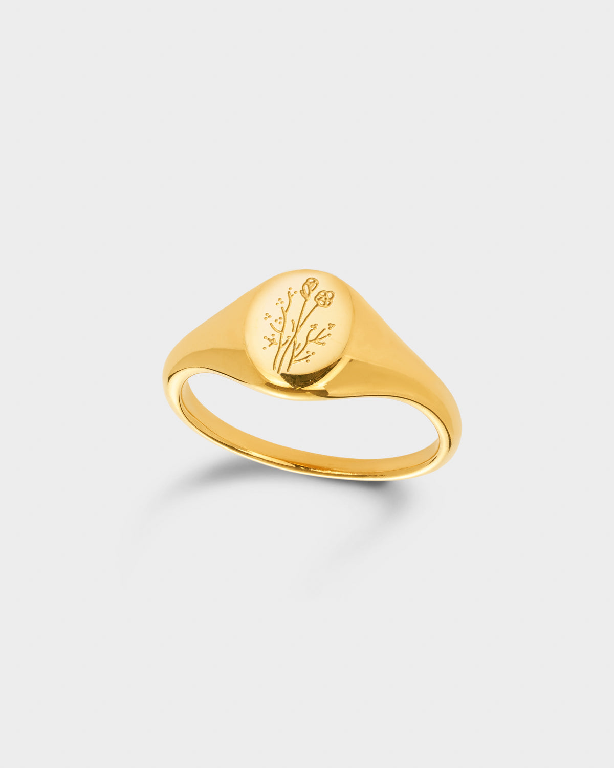 A polished yellow gold signet ring with an oval face engraved with a floral design.