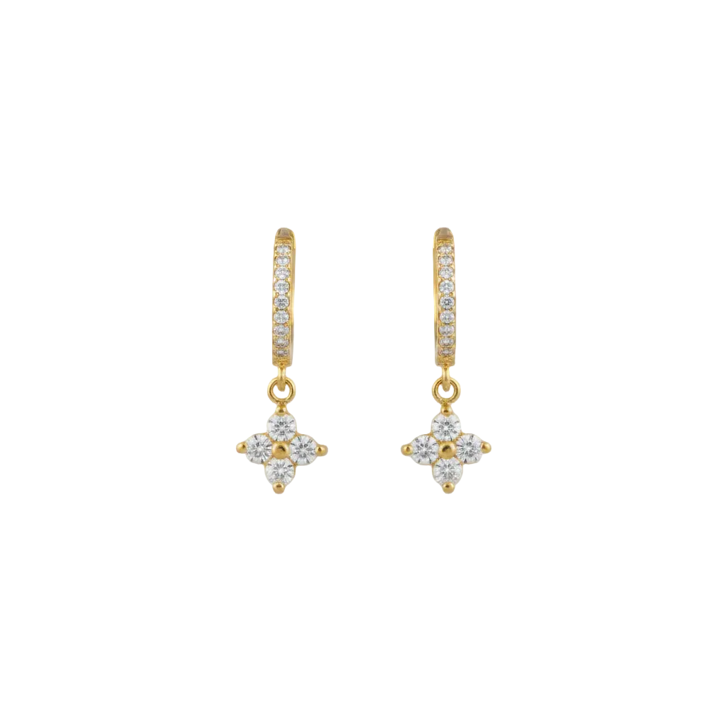 A gold huggie hoop earring with a dangling floral clover charm set with clear stones.