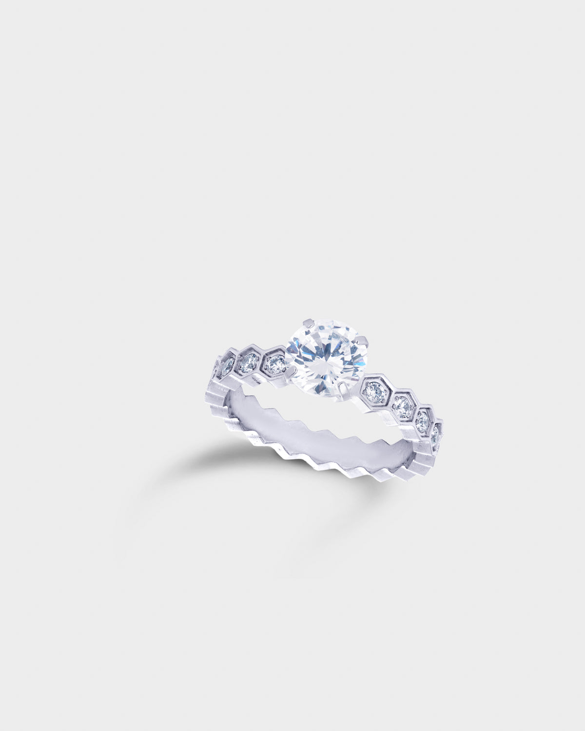A silver-toned eternity ring featuring a central round clear gemstone surrounded by a halo of small hexagonal-cut stones.
