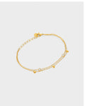 A delicate gold chain double layered bracelet featuring small dangling circle and heart charms.